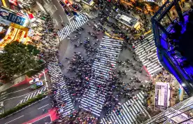 Aerial view of busy Shibuya crossing in Tokyo in-between large skyscrapers adorned with advertising screens, Japan