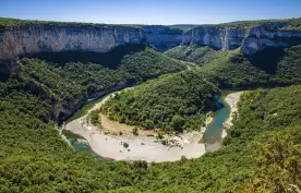 Curving Ardeche River, surrounded by tall trees and a cliff, France
