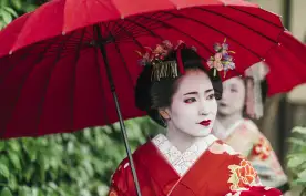 Beautiful Maiko with red clothing and umbrella in the streets of Kyoto, Japan