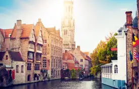 View of the waterfront buildings, canal and bell tower on a sunny day in Bruges, Belgium