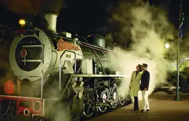 A mature couple looking at an old steam train at night