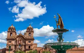 A golden fountain and an impressive religious building in Cuzco Main Square, Peru