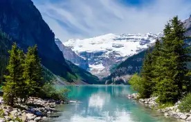 Beautiful Lake Louise with Victoria Glacier in the background and a glistening emerald lake. Several canoes can be seen at a distance on the lake.
