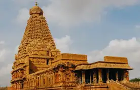 Hindu Temple showcasing Chola architectural style, built with a pyramid shaped spire. Stone steps lead to the entrance hidden under a column-supported roof