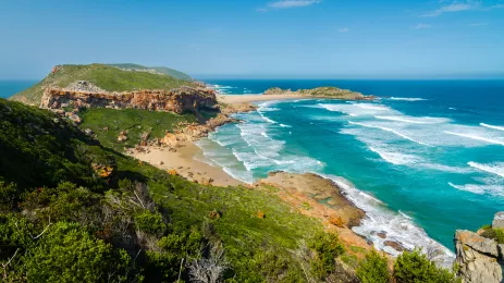 View of sandy bay and turquoise ocean from green hills behind.