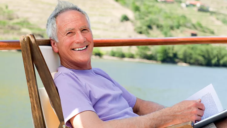 Smiling man relaxing in a chair while reading, on a boat deck