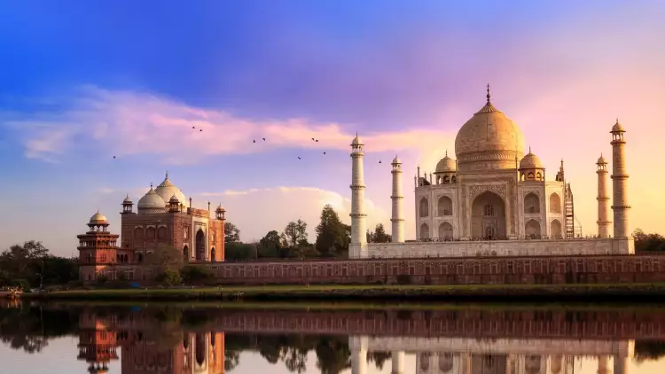 View of the Taj Mahal at sunset, it's image reflected in the water of a foreground lake.
