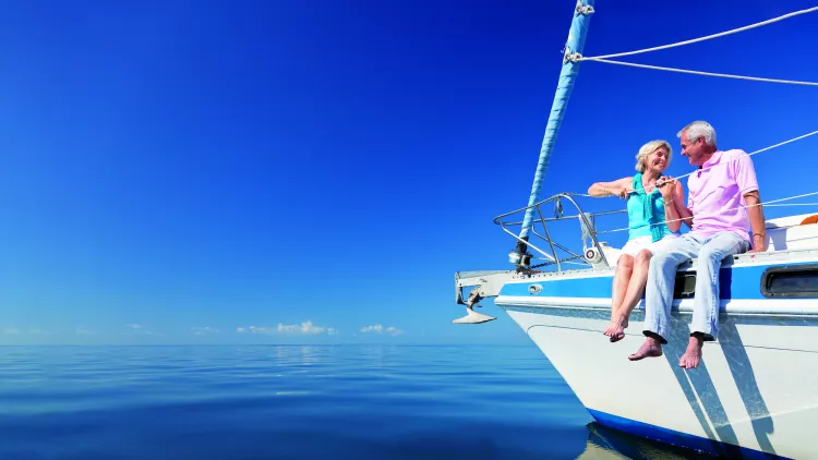 Happy senior couple sitting on the bow of a sail boat on a calm blue sea