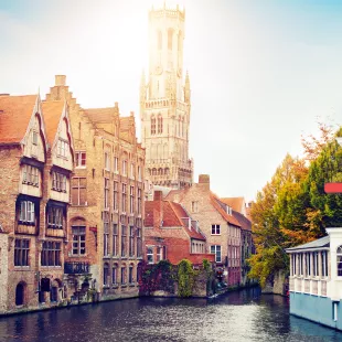 View of the waterfront buildings, canal and bell tower on a sunny day in Bruges, Belgium