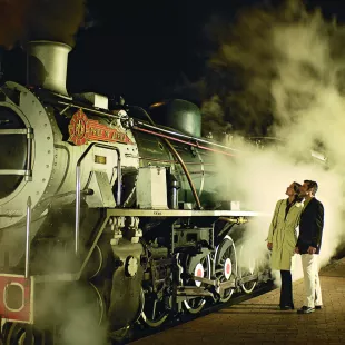 A mature couple looking at an old steam train at night