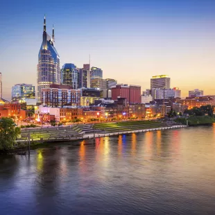 Nashville downtown skyline before sunset along a clear sky, it's reflection displayed in the foreground of the Cumberland River.