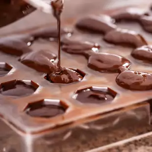 Close-up of chocolate being poured into a plastic mold to make praline