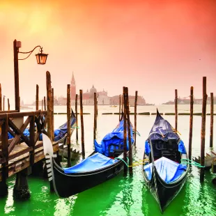 Venice canal boats lined up besides a dock under a warm sunset sky