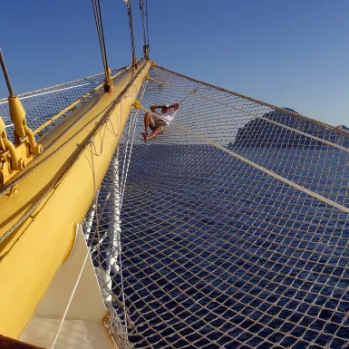 Man relaxing on the ship Bow netting in low afternoon sunlight