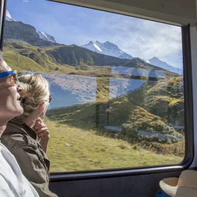 Mature couple in moving train enjoying the passing view of the Swiss alps and alpine area.