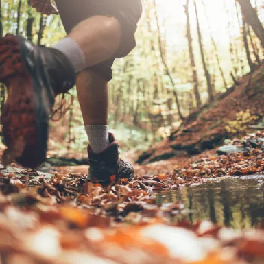 Close-up of hiker boots crossing mountain forest stream in autumn