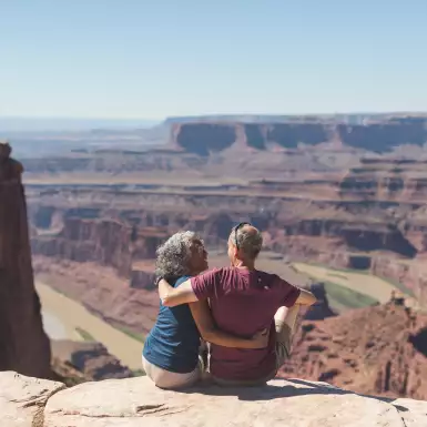 An mature couple sitting atop a canyon cliff edge, overlooking the valley below in Utah