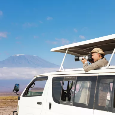 Professional photographer taking shots of Kilimanjaro mount aboard safari jeep, Kenya, Africa.