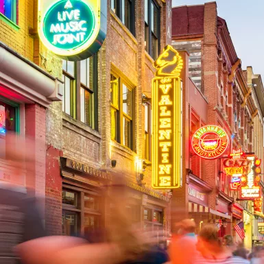 Broadway pub district with colourful neon signs in downtown Nashville, with blurred passing figures