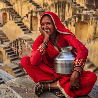 Indian woman in red clothing resting inside stepwell in village near Jaipur, Rajasthan, India.