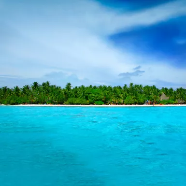 Stunningly turquoise and clear ocean waters surrounding Alimathà island with lush vegetation in the Maldives