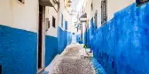 Narrow alley in Rabat Old Medina along a cobblestone pathway, walls painted in a stripe of white and blue, Morocco