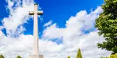 Large white cross headstone in front of rows of grave markers, inside the British cemetery by Ypres, Belgium