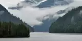 River surrounded by vegetation with mountains covered in misty clouds in Canada