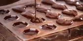 Close-up of chocolate being poured into a plastic mold to make praline