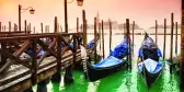 Venice canal boats lined up besides a dock under a warm sunset sky