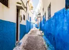 Narrow alley in Rabat Old Medina along a cobblestone pathway, walls painted in a stripe of white and blue, Morocco