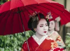 Beautiful Maiko with red clothing and umbrella in the streets of Kyoto, Japan