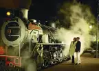 A mature couple looking at an old steam train at night
