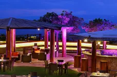 Patio terrace in the evening, lit by pink accent lights, with a bar and outdoor tables and seating visible, Jordan