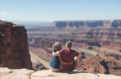 An mature couple sitting atop a canyon cliff edge, overlooking the valley below in Utah