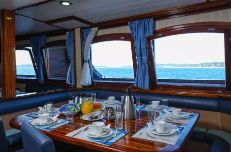 Internal shot of dining area within the Ms Mendula cruise yacht with glossy, dark wooden tables contrasting against dark blue furniture