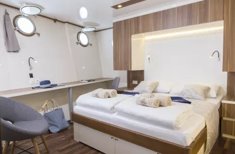 Double bed cabin with white decor with clean rolled and folded towels placed on the end of the made bed