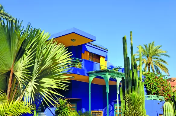 Vibrant yellow and blue house, with palm trees in front of it in Marrakech