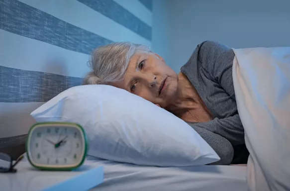 Senior woman lying awake in bed at night suffering from insomnia, with a worried facial expression.