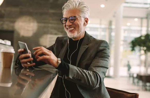 Mature businessman using phone and earphones at coffee shop