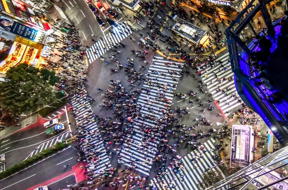 Aerial view of busy Shibuya crossing in Tokyo in-between large skyscrapers adorned with advertising screens, Japan