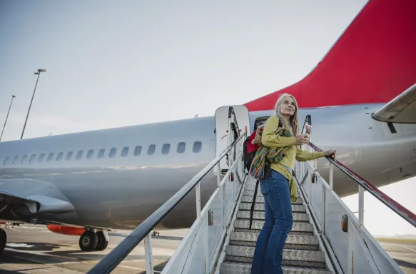 Senior woman standing on the air-stair of a plane with her boarding pass and has turned round to give one last look