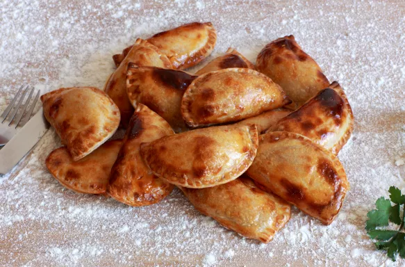 Close-up of an empanada, a turnover lightly dusted with icing sugar.