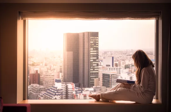 A woman in her pyjamas, looking out of her hotel window at the cityscape of Shibuya, Tokyo. 