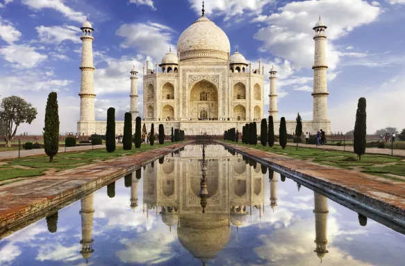 The Taj Mahal, monument of love, with it's image reflected in a decorative pool under a blue sky 