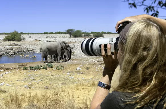 Photographer capturing a waterhole and wild animals in Etosha National Park, Namibia