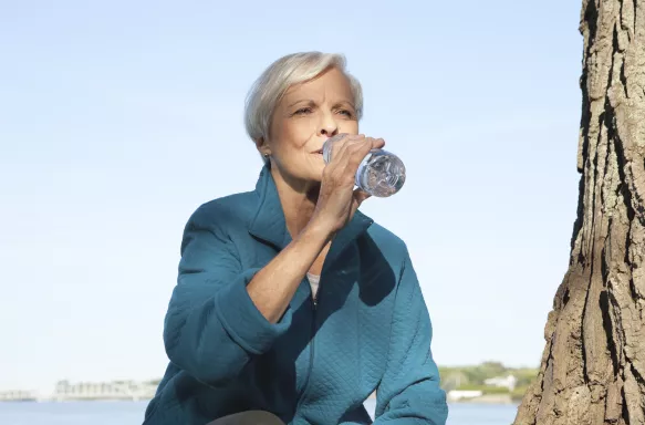 A senior woman taking a water break outside after exercising.