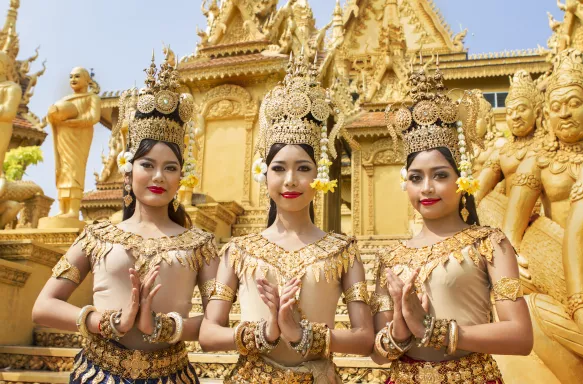 3 Apsara Cambodian dancers in traditional Apsara costumes greet in a temple courtyard.