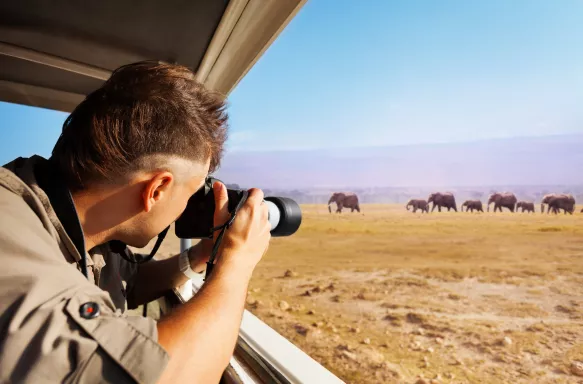 Man taking photo of herd of elephants during Great Migration from safari jeep, Kenya, Africa.