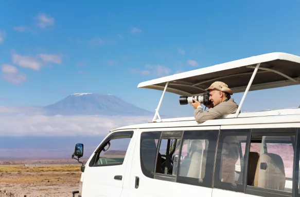 Professional photographer taking shots of Kilimanjaro mount aboard safari jeep, Kenya, Africa.